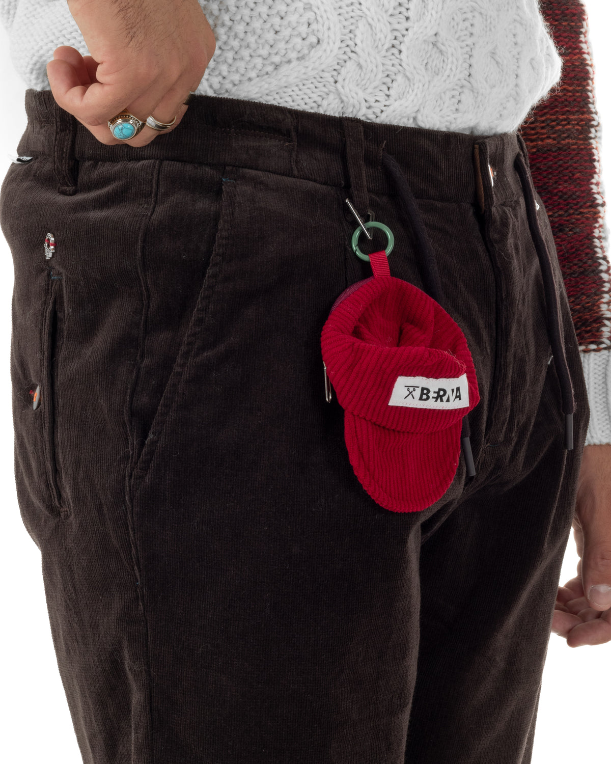 Coulisse e bottone sulla vita dei pantaloni marroni con accessorio rosso agganciato al passante.
